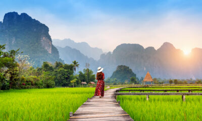 young-woman-walking-wooden-path-with-green-rice-field-vang-vieng-laos